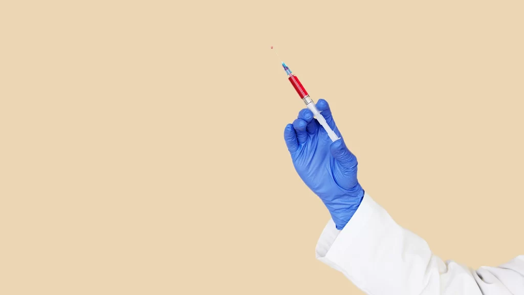A medically gloved hand holding a needle filled with stem cells, with a beige photo background.